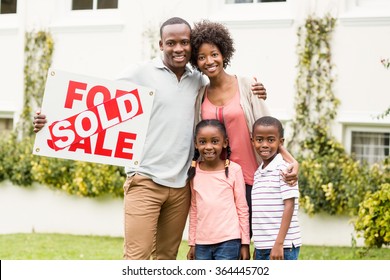 Happy Family Standing Together While Holding A Sold Sign