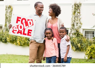 Happy Family Standing Together While Holding A Sold Sign