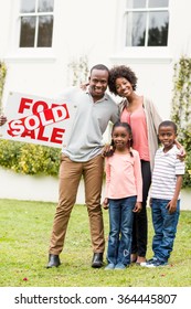 Happy Family Standing Together While Holding A Sold Sign