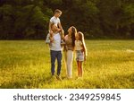 Happy family strolling in nature all together. Happy, joyful mother, father and little children walking on green grass in a beautiful park on a sunny summer evening