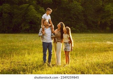Happy family strolling in nature all together. Happy, joyful mother, father and little children walking on green grass in a beautiful park on a sunny summer evening - Powered by Shutterstock
