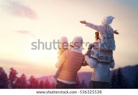 Happy family at sunset. Father, mother and two children daughters are having fun and playing on snowy winter walk in nature. The child sits on the shoulders of his father. Frost winter season.