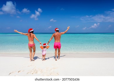 A happy family in swimsuits and with santa claus hats runs into the turquoise sea of a tropical paradise beach during their christmas holidays - Powered by Shutterstock