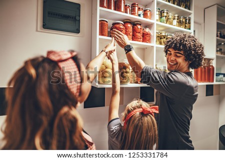 A happy family takes jars with pickled vegetables from the pantry shelf.