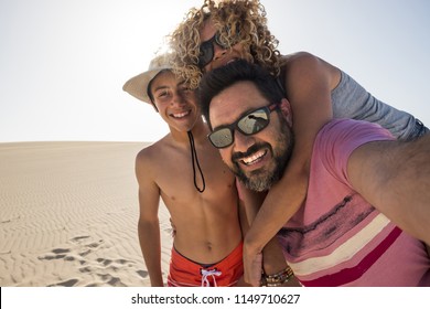 Happy Family Taking Selfie Picture On Vacation During The Summer Holiday At The Beach. Fuerteventura Desert And Three Caucasian People Having Fun And Joy Together. Love And Relationship. Travel