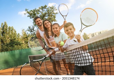 Happy Family With Tennis Rackets On Court Outdoors