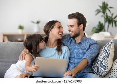 Happy family of three bonding using laptop sitting on couch at home, smiling parents with kid daughter having fun talking laughing relaxing with computer doing internet shopping together on weekend