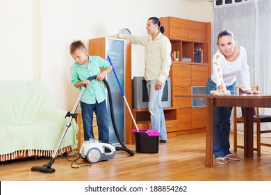 Happy Family Of Three With  Boy Cleaning With Vacuum Cleaner In Living Room