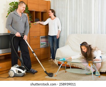 Happy Family Of Three Cleaning Up A Room All Together. Focus On Man