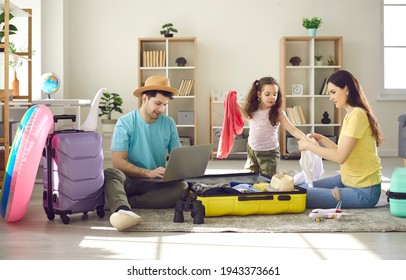 Happy Family Of Three Going To Travel. Father Choosing Tour, Buying Ticket Or Reserving Hotel Online Using Laptop. Mother With Preschool Daughter Packing Clothes In Suitcase Luggage Bag. Home Interior