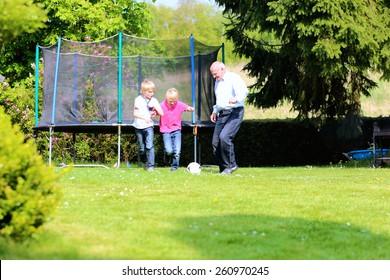 Happy Family Of Three, Healthy Grandfather With Laughing Grandsons, Twin Teenage Boys, Playing Soccer In The Garden At The Backyard Of The House On Sunny Summer Vacation Day