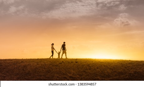 happy family of three holding hands walking together in a grass field at sunset - Powered by Shutterstock