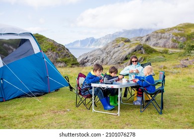 Happy family with three kids, wild camping in Norway summertime, people having breakfast adn coffee on a cliff next to a fjord in Lofoten, Norway