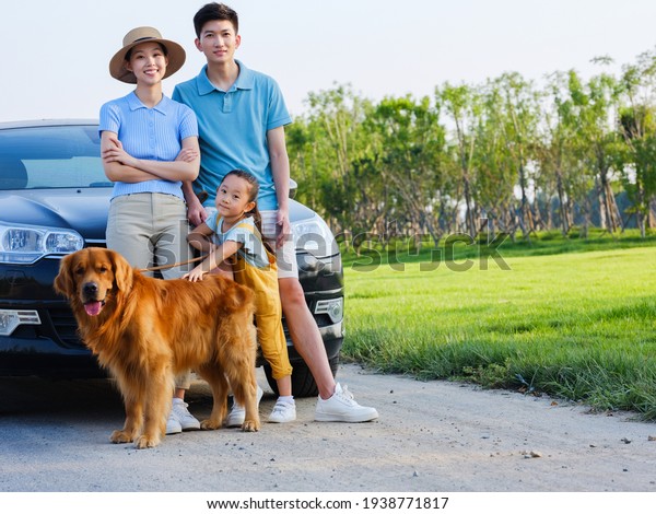 Happy family of three and pet dog in front of car in\
the park