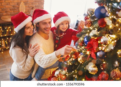 Happy family of three in Santa hats decorating Christmas tree with bubbles and bows at home - Powered by Shutterstock