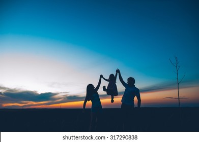 Happy family together, parents with their little child at sunset. Father raising baby up in the air.