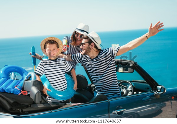 Happy family travel by car to the\
sea. People having fun in cabriolet. Summer vacation\
concept
