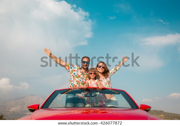 Happy family travel by\
car in the mountains. People having fun in red cabriolet. Summer\
vacation concept