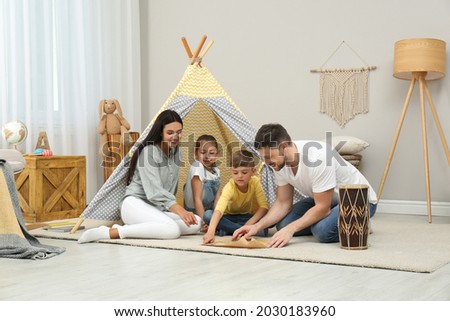 Happy family with treasure map near toy wigwam at home