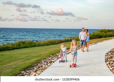 Happy family with two children: mom, dad and two daughters on scooters going on the oceanfront walkway, seascape, sky with clouds - Powered by Shutterstock