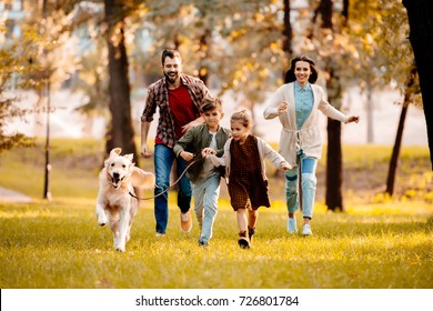 Happy family with two children running after a dog together in autumn park - Powered by Shutterstock