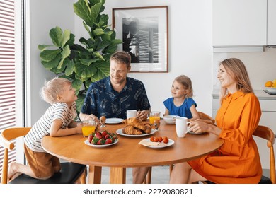 happy family with two children sitting by the table and eating breakfast in the morning at home kitchen - Powered by Shutterstock