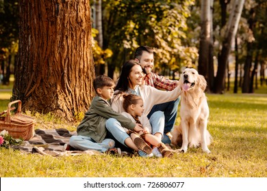 Happy family with two children sitting on a picnic blanket and petting a dog - Powered by Shutterstock