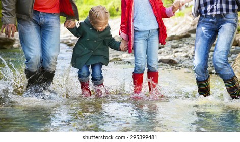 Happy Family With Two Children Wearing Rain Boots Jumping Into A Mountain River. Photo In Motion. DOF