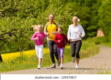 Happy Family With Two Girls Running Or Jogging For Sport And Better Fitness In A Meadow In Summer