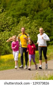 Happy Family With Two Girls Running Or Jogging For Sport And Better Fitness In A Meadow In Summer