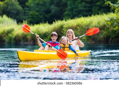 Happy Family With Two Kids Enjoying Kayak Ride On Beautiful River. Mother With Little Girl And Teenager Boy Kayaking On Hot Summer Day. Water Sport Fun. Canoe And Boat For Children