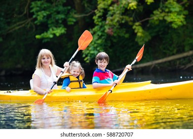 Happy family with two kids enjoying kayak ride on beautiful river. Mother with little girl and teenager boy kayaking on hot summer day. Water sport fun. Canoe and boat for children. - Powered by Shutterstock