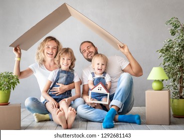 Happy Family With Two Kids Playing Into New Home. Father, Mother And Children Having Fun Together. Moving House Day And Real Estate Concept