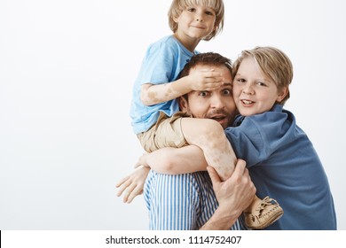 Happy Family Of Two Sons And Father Gazing And Smiling At Camera. Dad Holding Cute Kid With Vitiligo On Shoulders While Older Brother Hanging On Chest, Having Fun And Share Positive Emotions