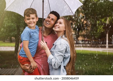 Happy Family With Umbrella Walking Under Rain In Park