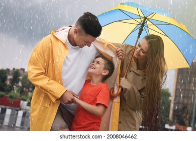 Happy Family With Umbrella Walking Under Rain On City Street