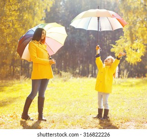 Happy Family With Umbrellas In Sunny Autumn Rainy Day, Mother And Child Enjoying Rain