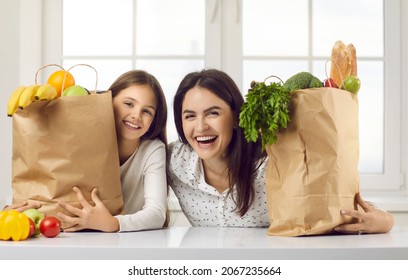 Happy Family Unpacking Groceries At Home. Portrait Of Cheerful Beautiful Mom And Kid At Kitchen Table Counter With Bags Full Of Apples, Oranges, Peppers, Tomatoes, Zucchinis, Parsley From Food Market