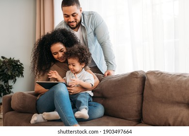 Happy family using digital tablet. Young parents looking how their son learning at home.