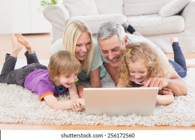 Happy family using laptop together while lying on rug at home - Powered by Shutterstock