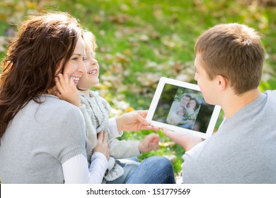 Happy Family Using Tablet PC Outdoors In Autumn Park