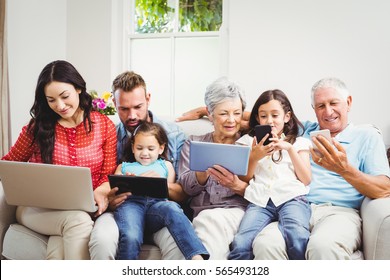 Happy family using technologies while sitting on sofa at home - Powered by Shutterstock