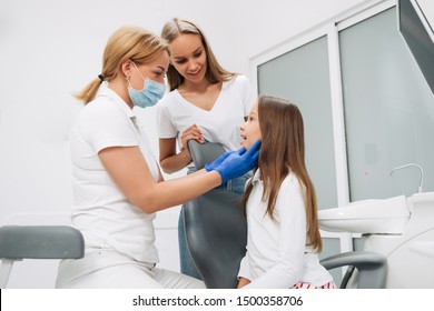 Happy Family At Visit In The Dentist Office. Female Dentist Checking Teeth The Little Girl, Her Mother Standing Next To Her.