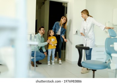 Happy Family At Visit In The Dentist Office. Female Dentist Greets The Patients Nicely And Shows The Girl Where To Sit.