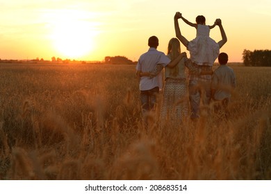 Happy Family Walking In Field And Looking At Sunset