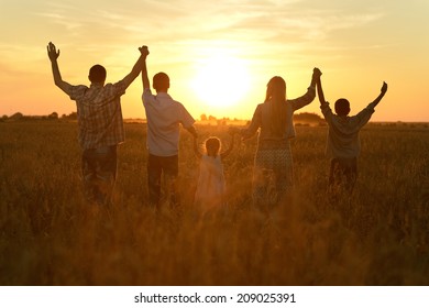 Happy Family Walking In Field On Sunset And Holding Hands