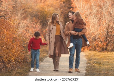 Happy Family Walking And Laughing  In The Fall Park. Portrait Of A Caucasian Mother And Father With Their Children In Beautiful Outfits On A Sunny Autumn Day In Forest. Family Lifestyle Concept.