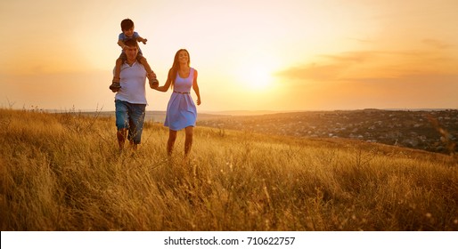 Happy Family Walking On Field In Nature At Sunset