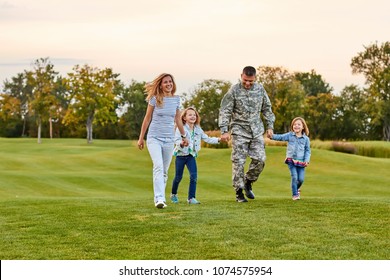 Happy family walking on the grass. Soldier with his wife and daughters in the park.