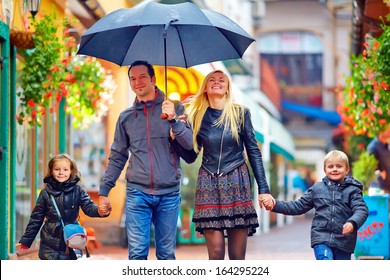 Happy Family Walking Under The Rain On Colorful Street